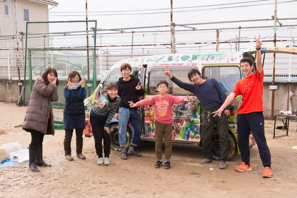 写真：ペイントした車（プレーカー）の前でポーズを取る子どもと、「遊び場を考える会」のスタッフ