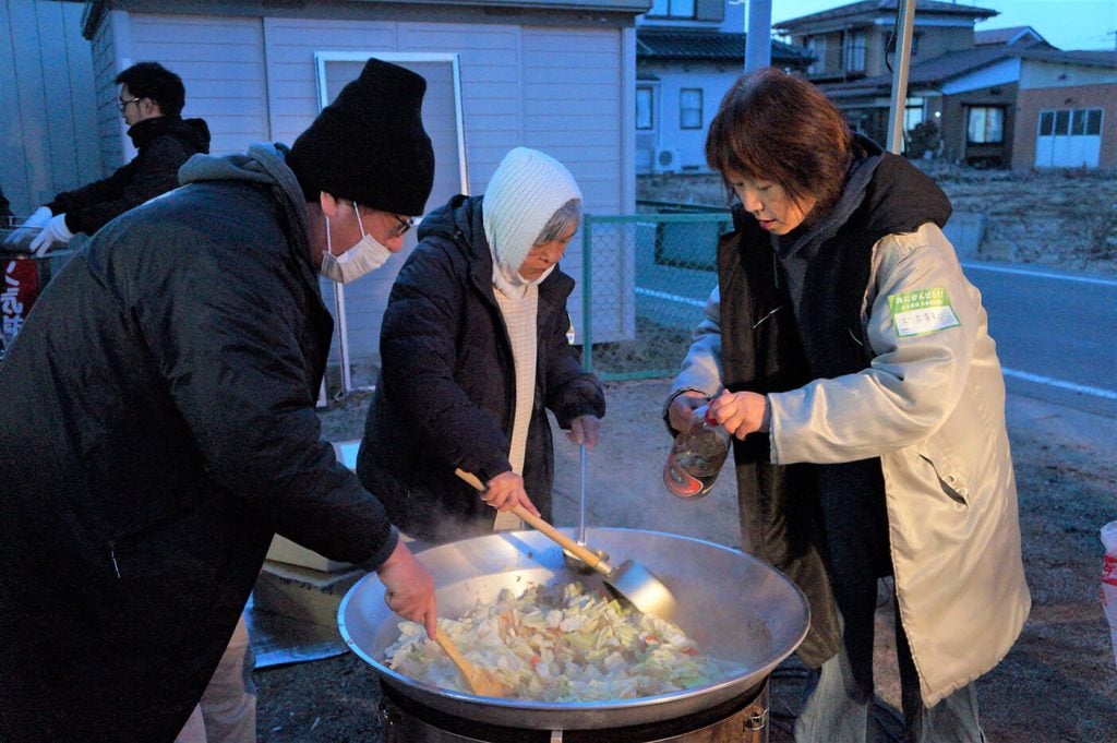 写真：毎週金曜日、金山保育園の前で開かれている炊き出しの様子。支援団体のメンバーら3人が、野菜が入った大きな鍋を囲んでいます