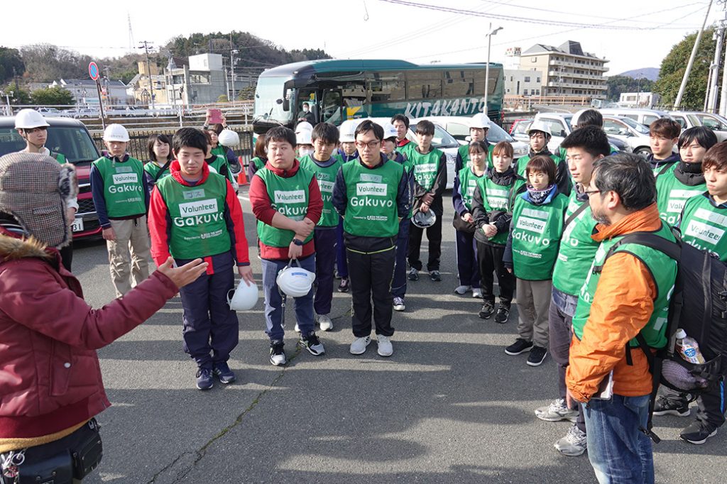 写真：駐車場で担当者からボランティアの注意事項などを説明される大学生たち 