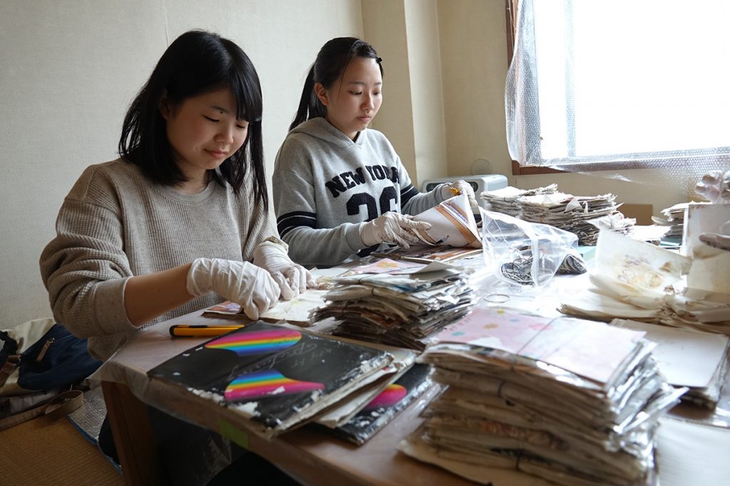 写真：テーブルの上に、水に浸かったアルバムを並べて、写真を切り出す立川さんたちの様子 