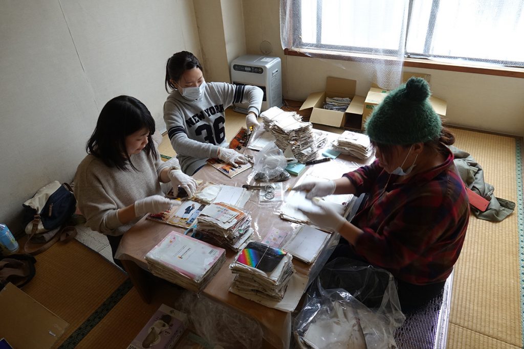 写真：テーブルの上に、水に浸かったアルバムを並べて、写真を切り出す3人のボランティア 