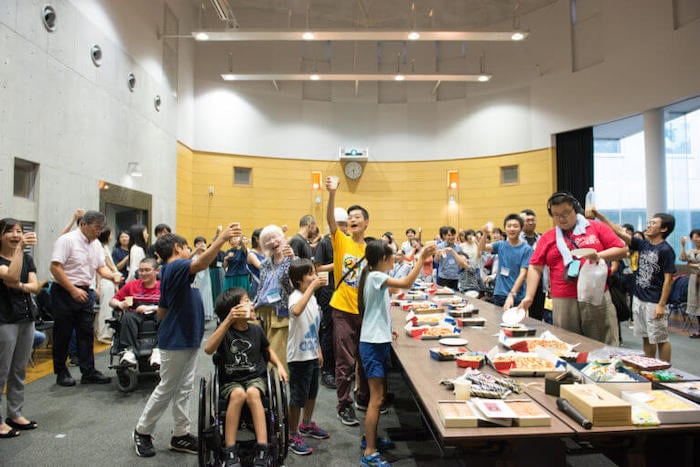 写真：講義室の中で飲み物や食べ物を楽しみながら、乾杯などして盛り上がるたくさんのスカラー、講師たち