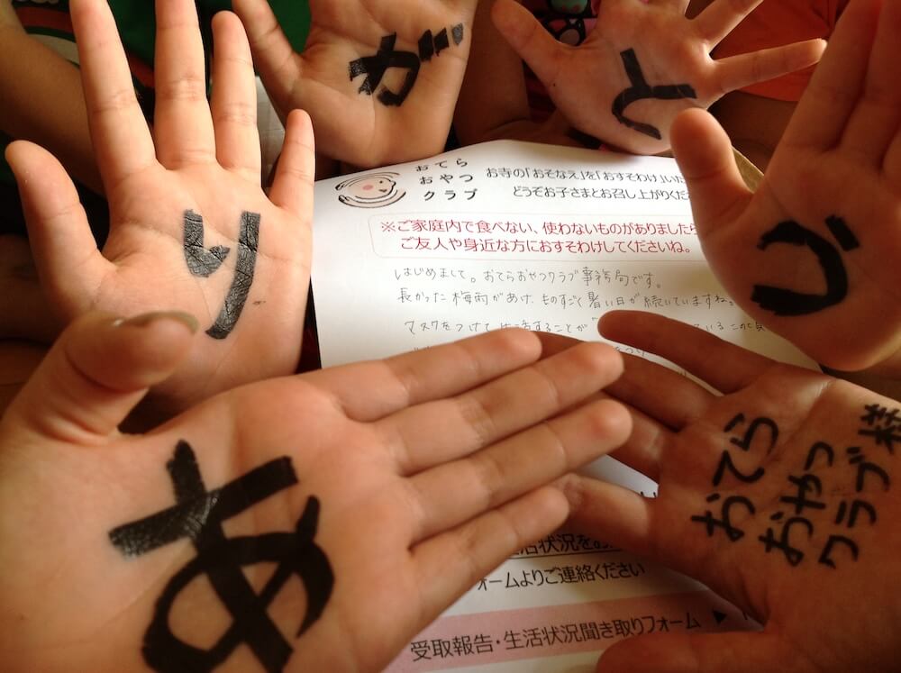 写真:子どもたちの手のひらに書かれた「ありがとう、おてらおやつクラブ」の文字