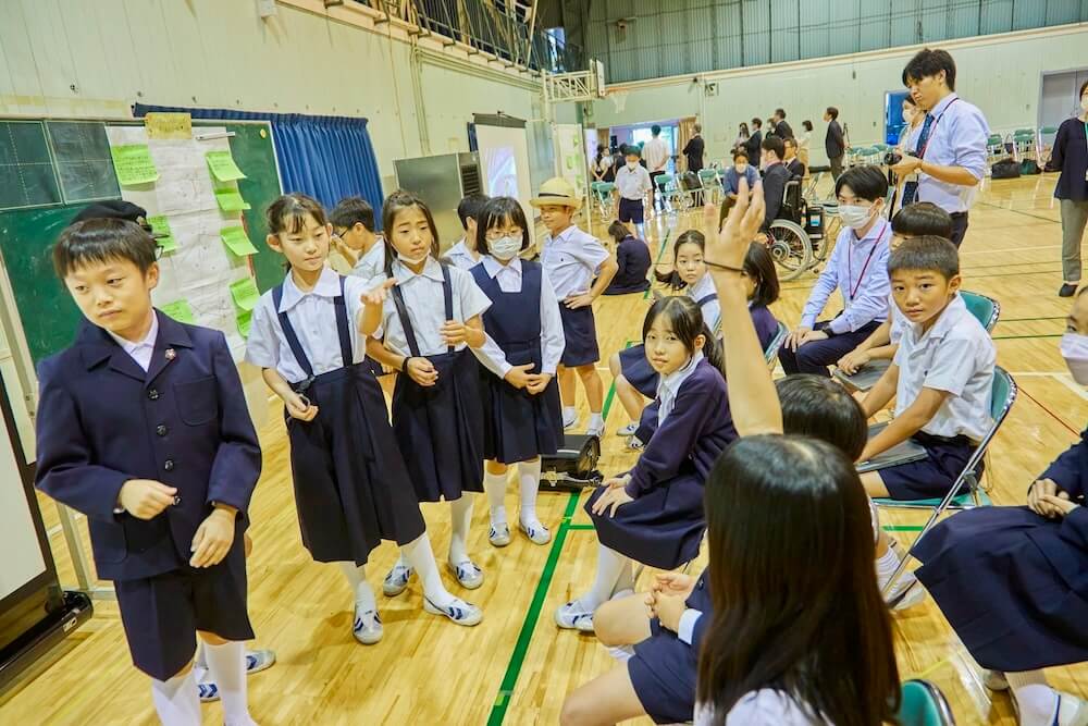 写真:アイデアを発表する児童たちに手を挙げて質問をしようとする児童