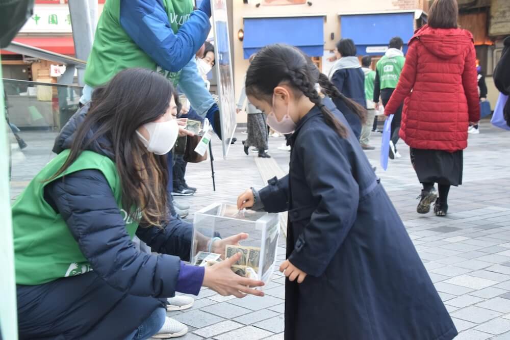 写真：ボランティアが持つ募金箱にお金を寄付する少女