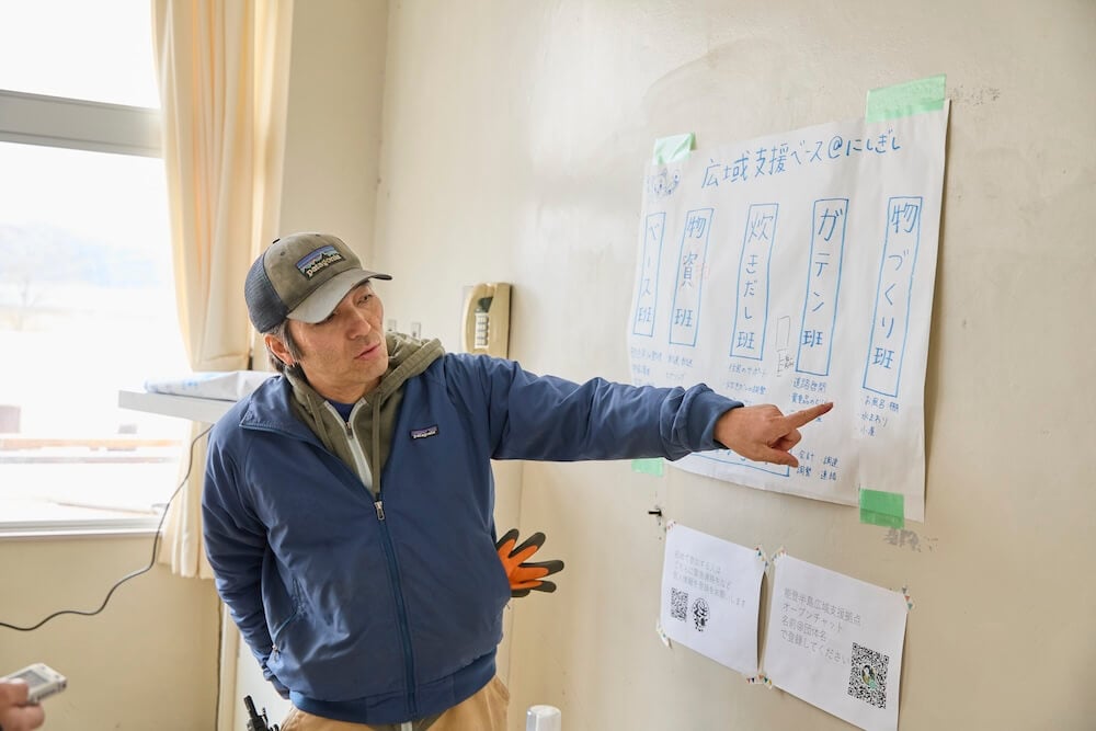写真：壁に貼られた、役割ごとに区切られた「班」について、指を指しながら説明する吉村さん