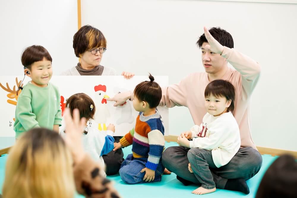 手話で絵を説明する久保沢さんの周りに集まる子どもたち。中には膝の上に乗る子どもの姿も