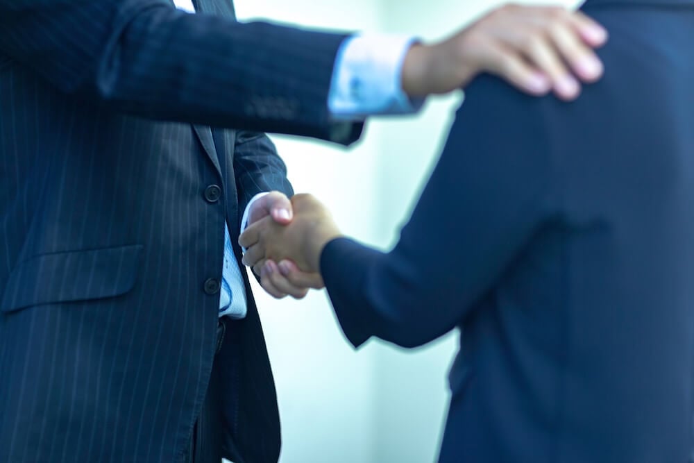 イメージ：握手しながら、もう一方の手を肩に手をかける、部下を労う上司