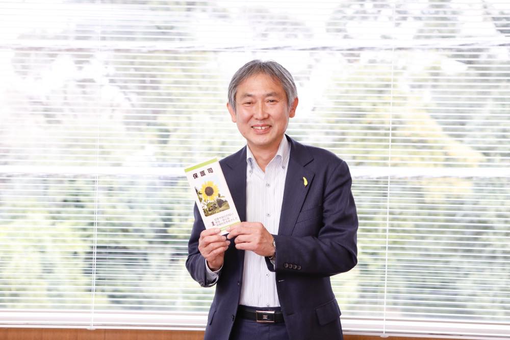 窓際に立つ吉田さん。保護司のパンフレットを持っている