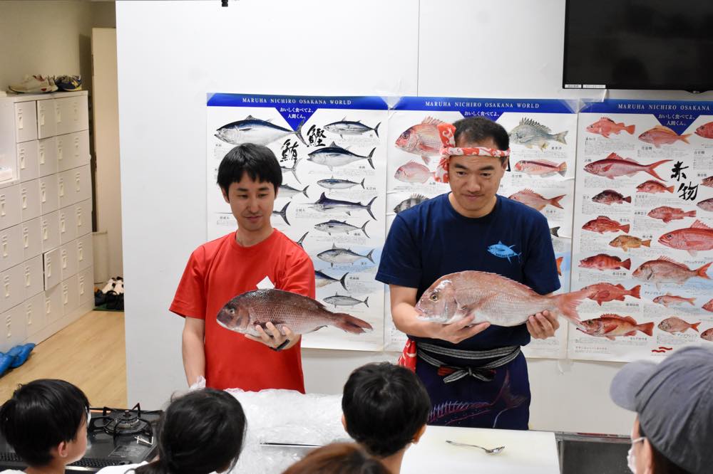 たくさんの子どもたちに対し、手に持った魚に関する話をする早武さんとスタッフ
