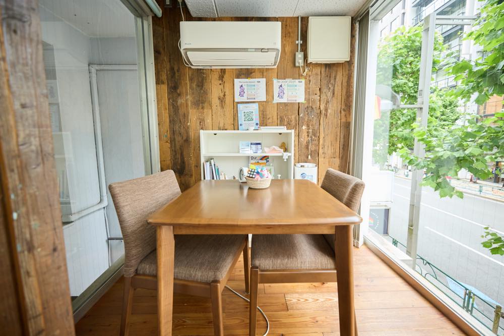 ラップアラウンド・サポート用の個室の様子。道路と階段側に大きな窓があり、自然光が差し込んでいる。相談時にはカーテンで窓を閉めてプライバシーを保つ。部屋の中央には向かい合う形で机と椅子が2脚配置されている。