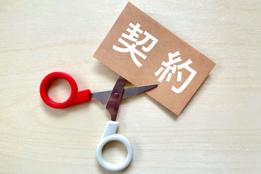 「契約」と書かれた紙を、真ん中からハサミでカットする、契約破断をイメージした画像