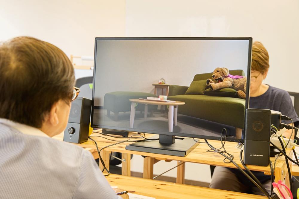 人が席に座り、モニターを見ている。モニターには「つなっぐ」の司法面接室の様子が映し出されている。