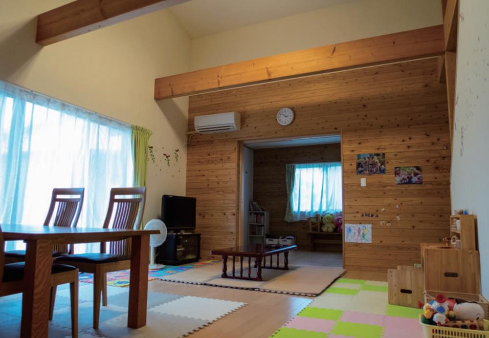 「子どもショートステイ」専用の家の内観。木を基調としたリビングダイニングルーム。木製のダイニングテーブルと椅子、テレビなどが置かれている