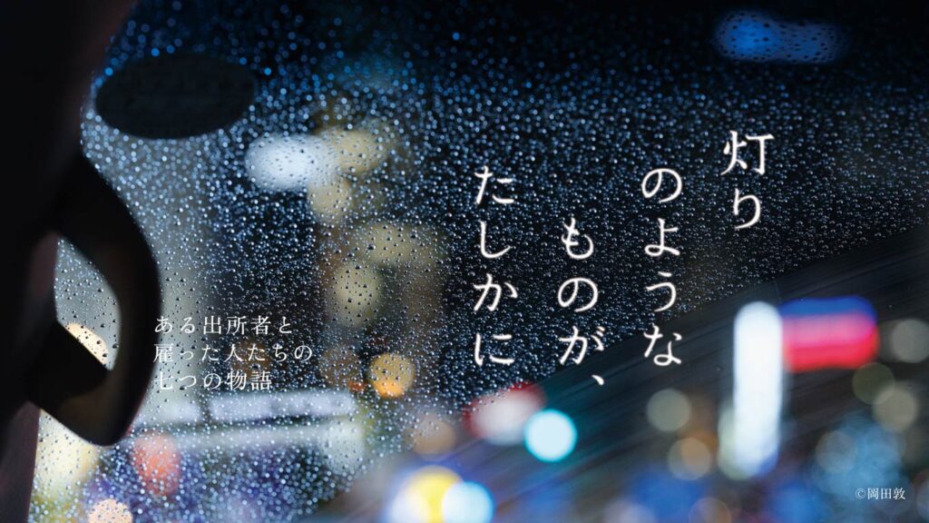 画像：職親プロジェクトドキュメンタリーシリーズの1シーン。画面中央に「灯りのようなものが、たしかに」の文字、画面左下に「ある出所者と雇った人たちの七つの物語」の文字、画像右下に「©岡田敦」の文字。