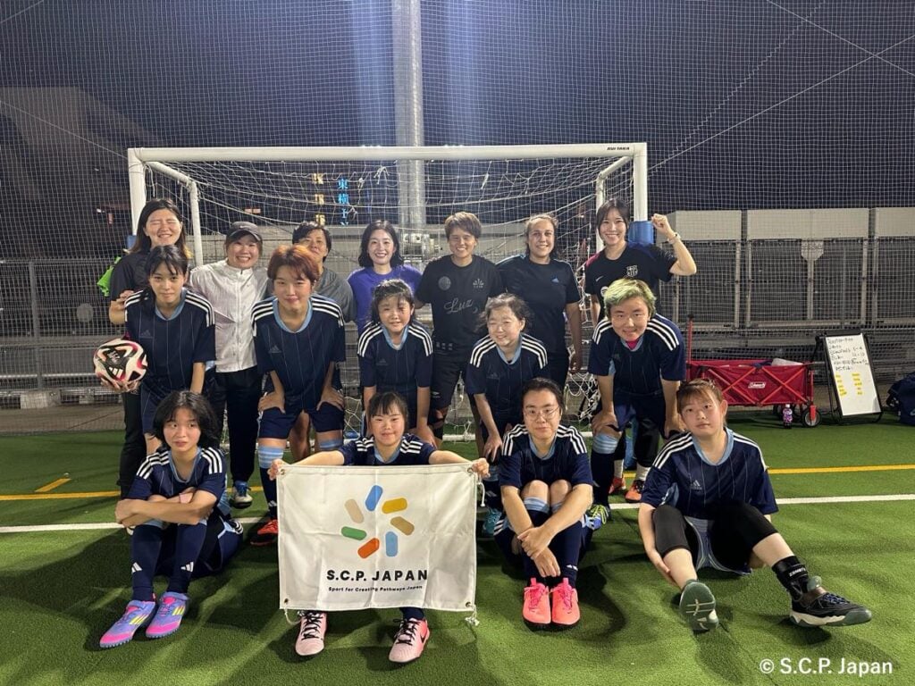 「FC RESIA」の集合写真。手前には「S.C.P. JAPAN」のロゴの旗が掲げられている。