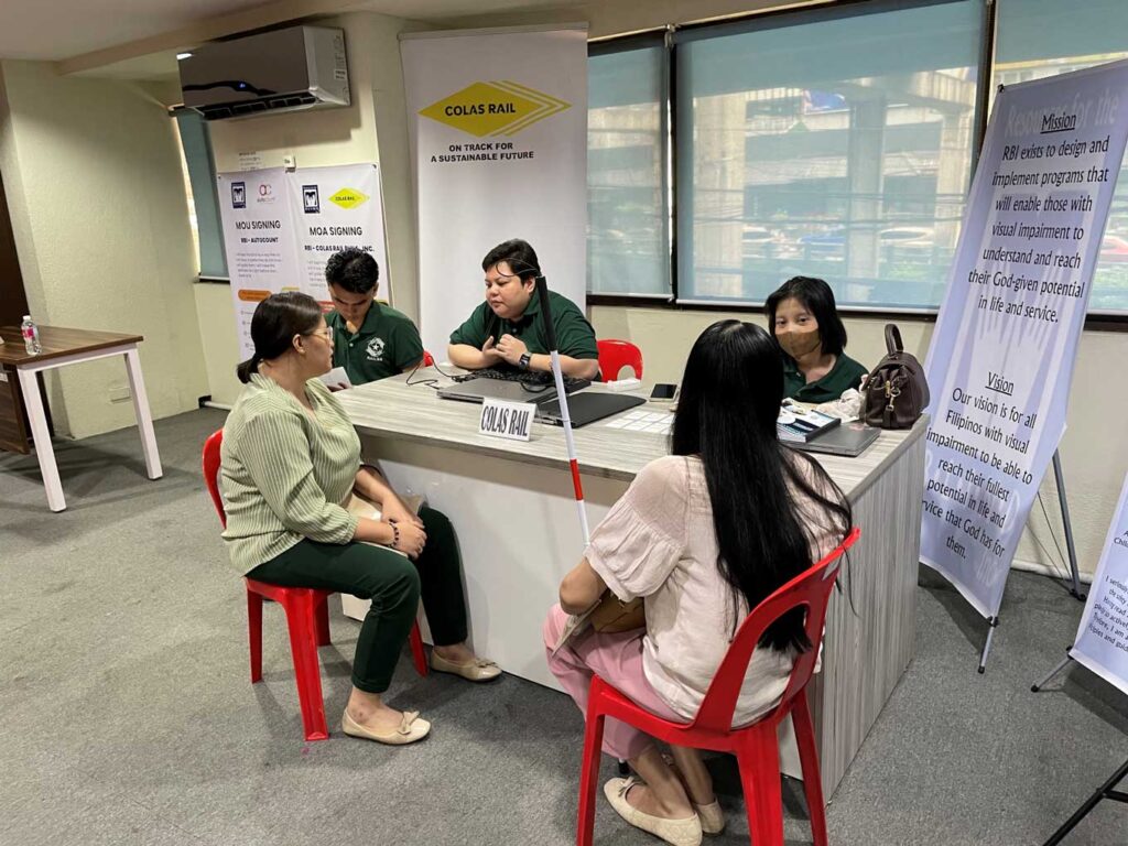 写真：企業ブースで視覚障害のある参加者と担当者が向かい合い、就職のための面接を行っている様子。